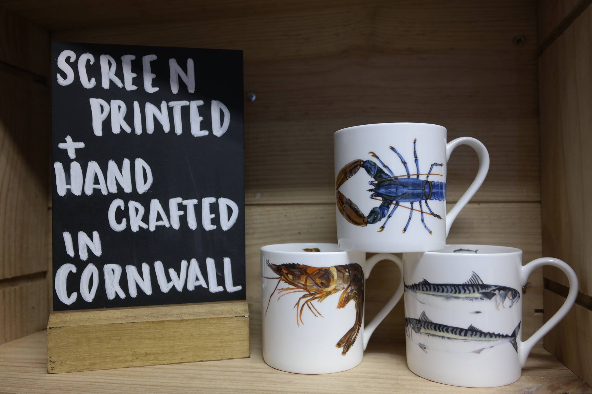 Mugs printed with lobster and crab designs beside a hand-lettered sign
