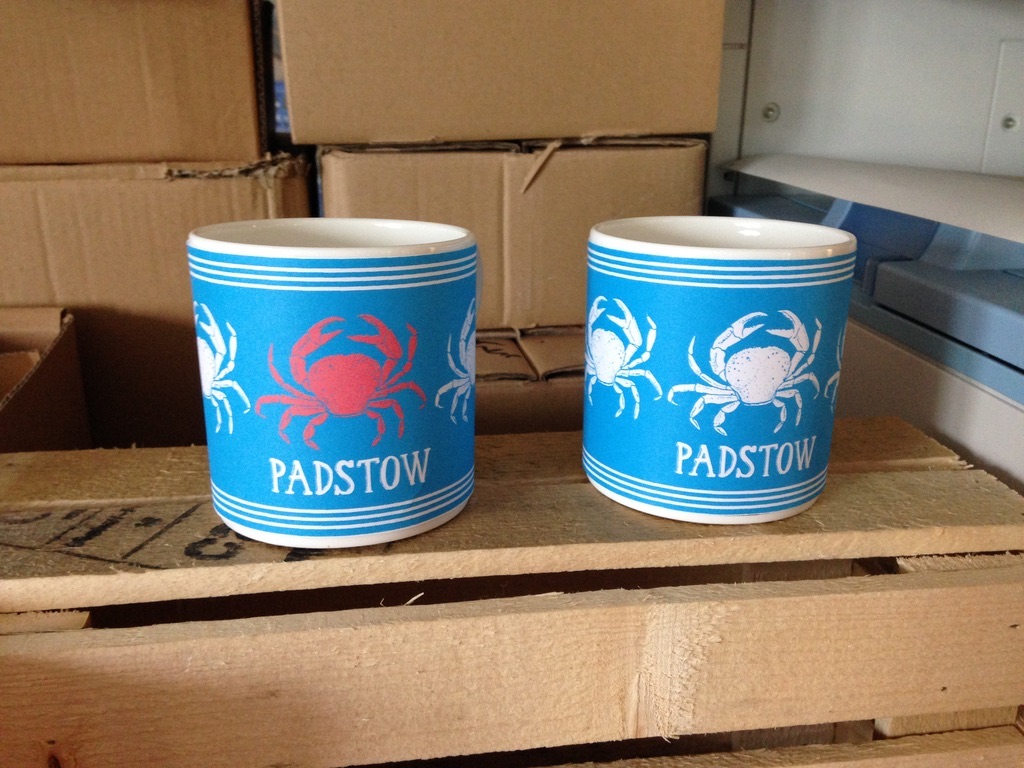 Turquoise mugs printed with a red crab and Padstow lettering