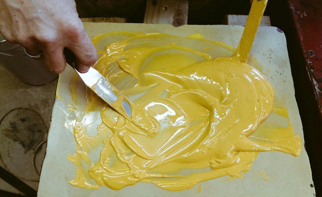 Yellow ceramic colour being mixed by hand with a palette knife